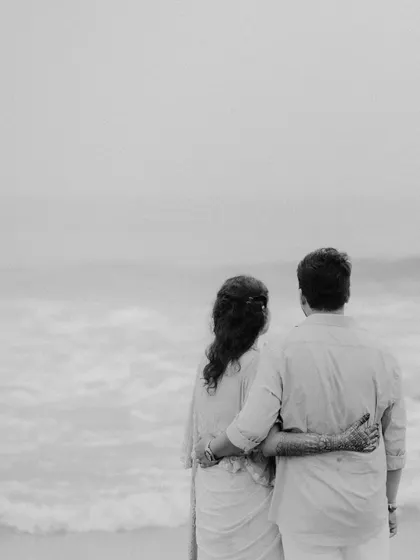 A timeless black and white photo of the couple looking out at the ocean, their arms around each other in a quiet moment of togetherness.