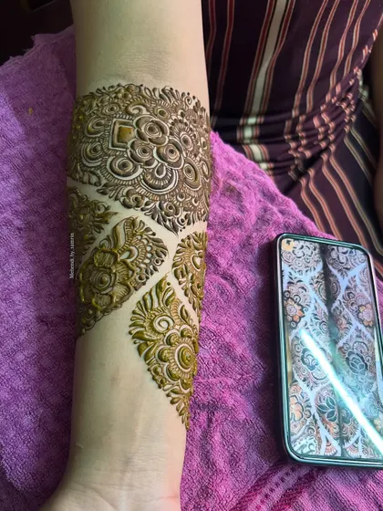 A close-up of the forearm, showing the intricate details of the designer pattern. The reference photo is visible on the phone.