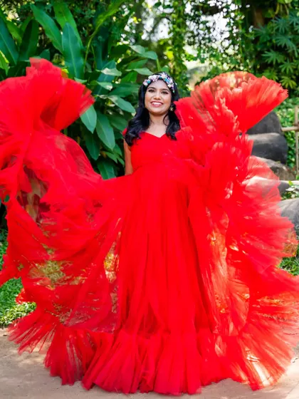 A joyful, vibrant portrait. The mom-to-be is surrounded by the ruffles of her bright red gown, looking like a beautiful flower in bloom.