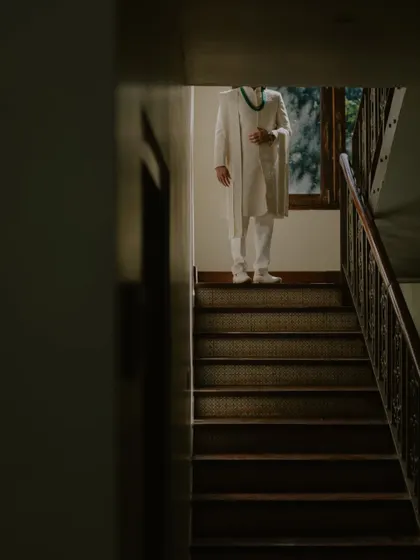 An artistic shot of the groom standing on a staircase, using shadows and light to create a dramatic and pensive portrait.