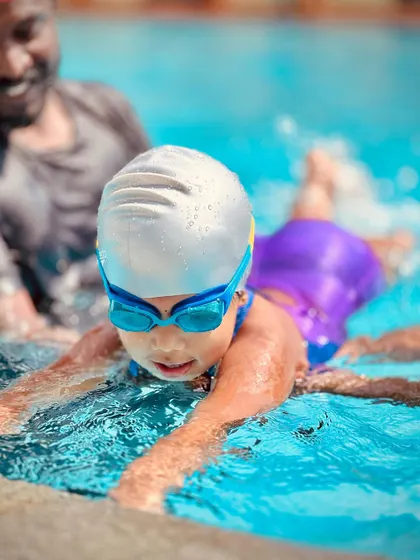 Practicing the correct body position for swimming starts early. Here, a coach helps a toddler with her form, building a strong foundation for future strokes.