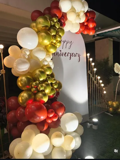 An elegant anniversary decoration with a white backdrop panel and a balloon garland in red, gold, and white.