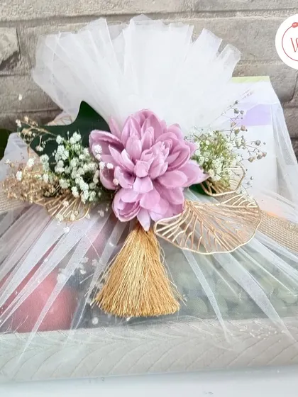 A stunning hamper in purple and white, featuring a mix of traditional treats and a modern Armani Exchange watch. The gift is elegantly wrapped in white tulle with a large purple flower.