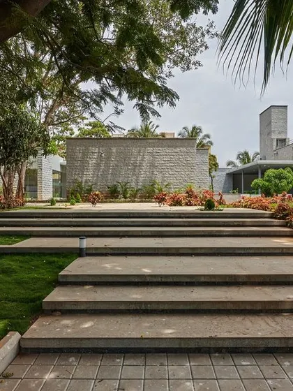 The landscape design at KIPCER includes gentle steps and ramps that navigate the site's terrain, leading towards buildings clad in locally sourced grey granite.