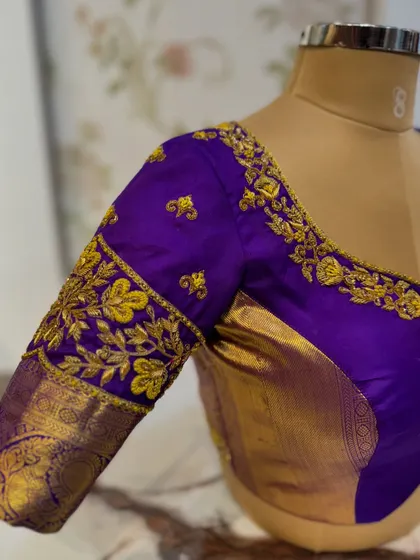 A rich purple blouse with gold floral embroidery on the sleeves and neckline, paired with a traditional Kanjeevaram zari border.