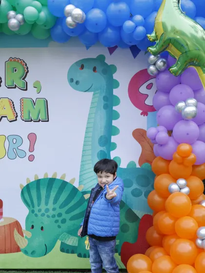 A young guest strikes a pose at a dinosaur-themed birthday party. Our vibrant backdrops and colorful balloon arrangements are perfect for creating a fun, prehistoric jungle vibe.
