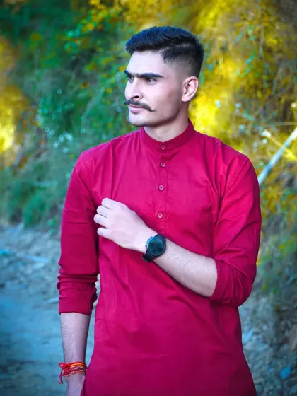 A stylish portrait of the groom against a backdrop of yellow foliage. The contrast between his red kurta and the background makes this a visually striking image.