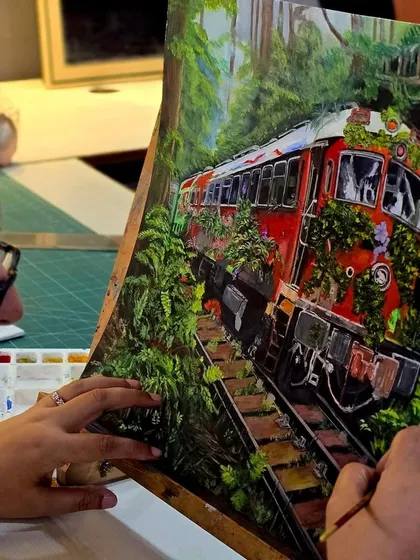 A student works on her detailed gouache painting, carefully adding leaves and foliage to the train.