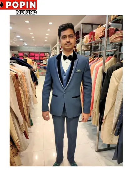 A client getting fitted in a blue three-piece tuxedo with a black velvet lapel. You can see the wide selection of traditional wear on the racks behind him.