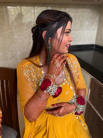 A happy, candid moment. Her hair is pulled back neatly, and the floral jewelry on her hands completes the Haldi look.