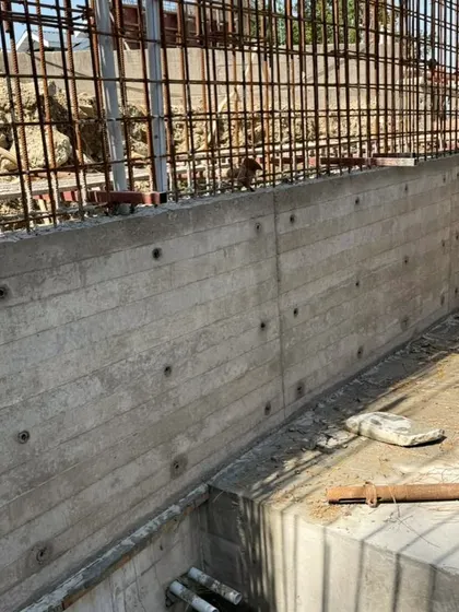 A board-formed concrete wall under construction. The wooden planks used in the formwork leave their grain imprinted on the concrete, adding a layer of natural texture.