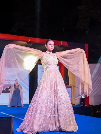 A model gracefully displays a flowing gown with dramatic, wing-like sleeves on the runway.