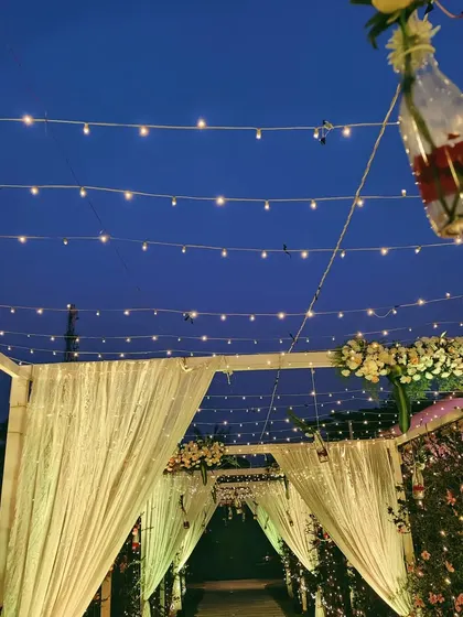 An enchanting pathway for a wedding reception at dusk. The entrance is framed by shimmering drapes and illuminated by strings of fairy lights against the deep blue evening sky.
