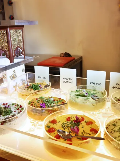 A beautifully lit display of our hummus and mezze bar. We offer a wide range of dips, from classic avocado hummus to peri-peri and baba ghanoush, all garnished with fresh herbs and edible flowers.