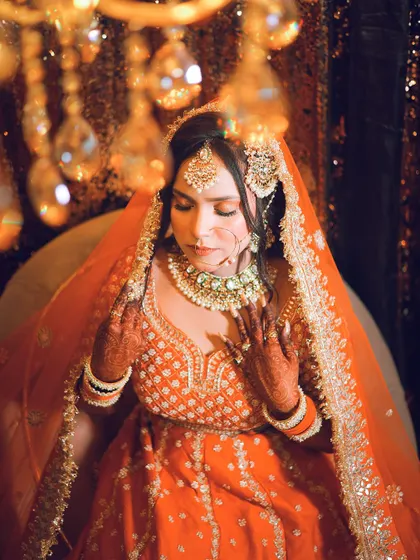 An artistic bridal portrait using warm, dramatic lighting from a chandelier to create a beautiful glow. The orange lehenga looks stunning in this light.