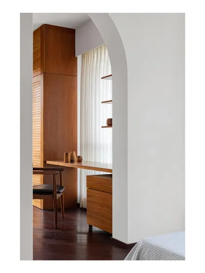 A view into the dedicated study area, framed by the arch. The custom teak desk and storage are designed to be both highly functional and aesthetically warm, creating a cozy corner for work.