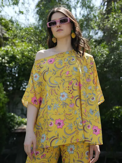 A bright yellow floral top and pants set, styled with modern pink sunglasses. The bold colors and sunny setting create a cheerful and eye-catching image for a summer campaign.