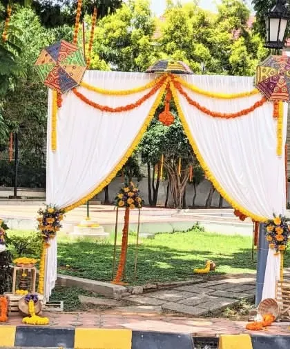 An outdoor entrance arch for a Mundan or other ceremony. The white drapes are accented with marigold garlands, and the welcome sign is placed at the entrance.