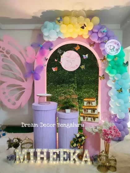 A 'Half way to one' celebration with a butterfly theme. The pink and purple arches against a grass wall create a beautiful garden-like setting.
