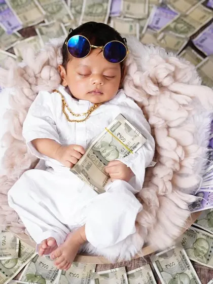 A fun and creative "youngest richest baby" themed shoot, with a newborn in a Marwari-style outfit surrounded by prop money.