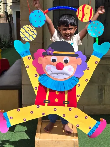 A young boy peeks out from behind a large, colorful clown craft. This large-scale project was a fun group activity that brightened up our outdoor space.