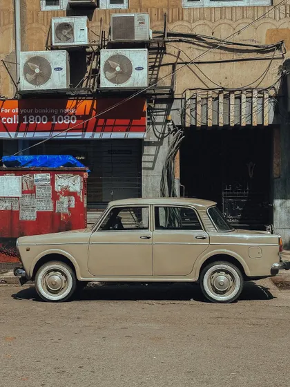A side profile of a vintage Fiat, showcasing its simple, classic design against a gritty, urban background.