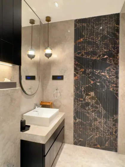 This bathroom combines classic and modern elements. A dark, fluted marble panel creates a dramatic accent wall behind the sink, while minimalist pendant lights and a sleek vanity complete the sophisticated look.
