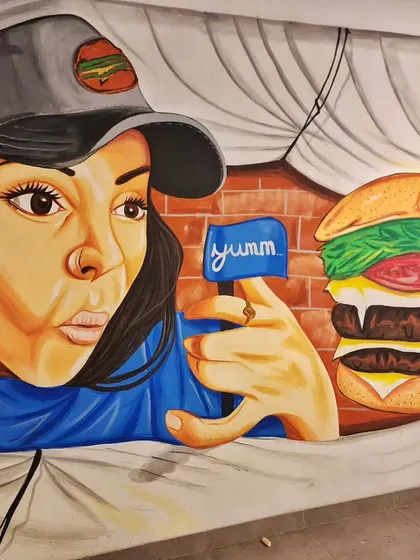A close-up of the burger mural, showing the "Yumm" sign and the illusion of the wall being pulled back.