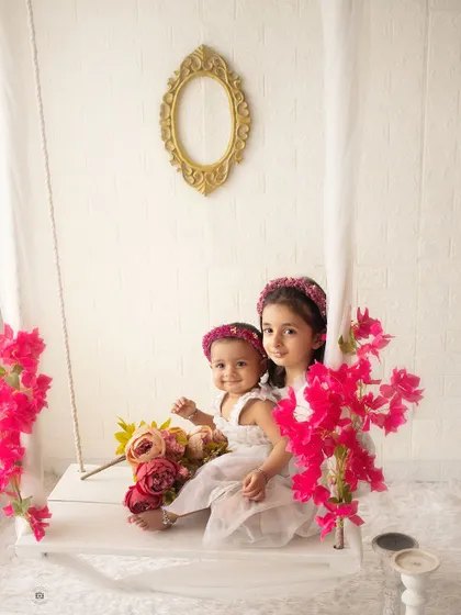 Two beautiful sisters sitting on our studio swing. The bright flowers and their sweet interaction create a whimsical and lovely sibling portrait.