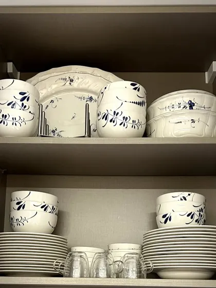 This crockery cabinet features a beautiful set of blue and white dinnerware. By stacking plates and arranging bowls neatly, the collection is both protected and displayed elegantly.