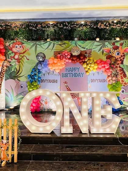 The main stage for a twins' first birthday, with a colorful jungle backdrop, animal cutouts, and a large light-up "ONE".