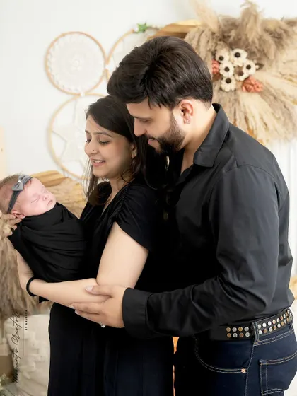 A quiet moment with a new family. The parents, dressed in black, look down at their sleeping newborn daughter, creating a simple and intimate portrait.