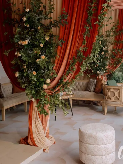 A beautiful lounge area where peach-colored drapes meet lush green floral pillars. The mix of textures and colors creates a warm and inviting space for guests.