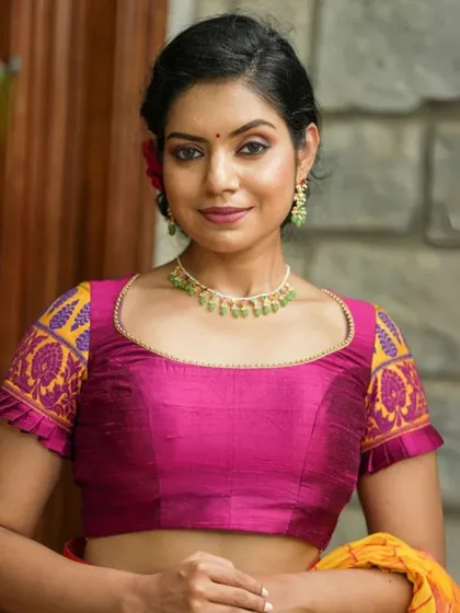 A bright pink blouse with contrasting yellow embroidered sleeves is paired with a simple green beaded necklace for a colorful and festive look.
