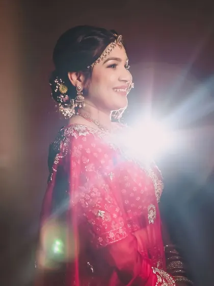 An artistic shot with lens flare highlighting the bride's joyful profile. Her hairstyle includes a floral bun, adding a touch of traditional freshness to the look.