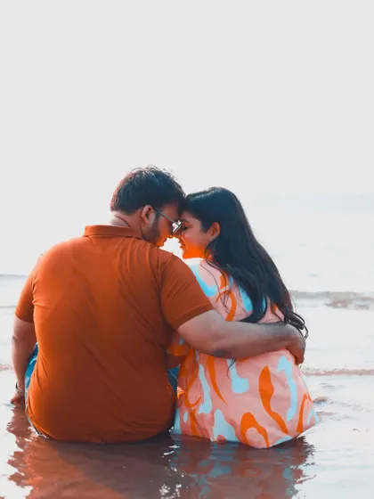 A tender moment of a couple sitting in the water at the beach, with a bright, minimalist background.
