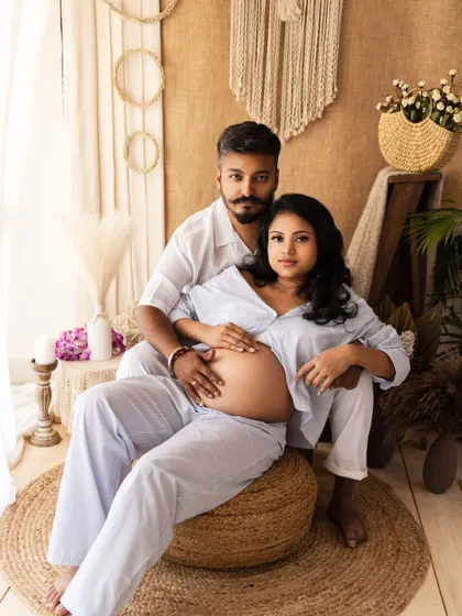 A stylish and relaxed maternity portrait in a boho setting. The couple's casual outfits and the natural studio decor create a modern and authentic feel.