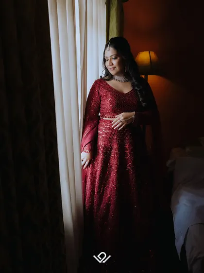 A bride in a red gown stands by a window, the soft light creating a beautiful and pensive portrait.