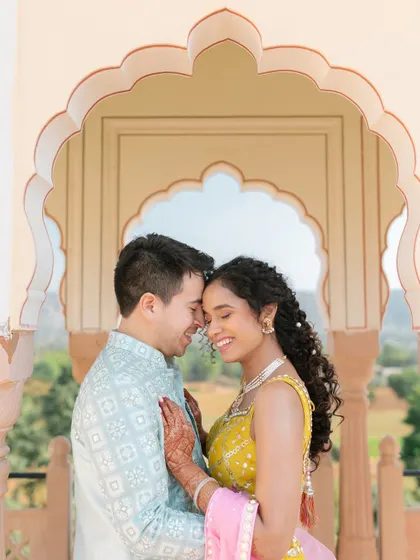 A sweet and intimate pre-wedding moment, with the couple sharing a happy embrace under a traditional Rajasthani archway.