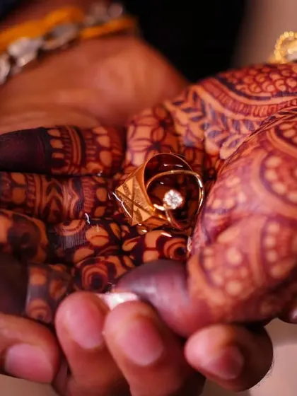 A close-up, artistic shot of the bride and groom's hands, showing the rich stain of the bridal mehendi holding the wedding ring.