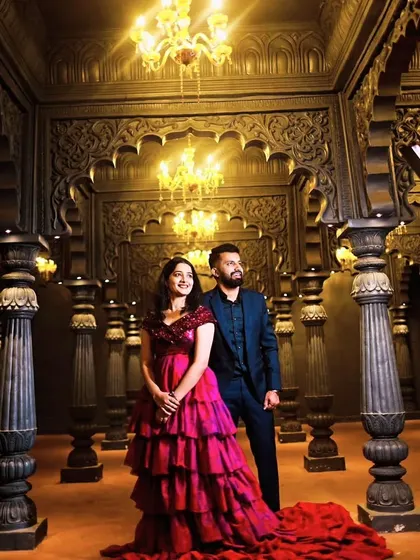 Posed in a grand, ornate room, this couple looks like royalty. Her pink and red tiered gown is perfectly complemented by his dark suit.