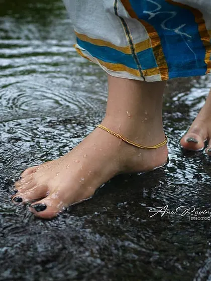 A close-up shot of a woman's feet, adorned with an anklet, standing in shallow, rippling water. This evocative image, with the traditional saree border visible, hints at a larger cultural story.