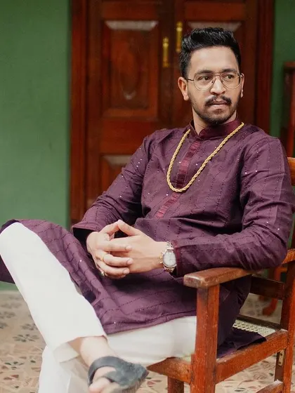 The groom, in a deep purple kurta, sits in an antique chair on the verandah, a regal and contemplative portrait.