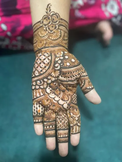 A single hand adorned with intricate work, featuring a floral cuff and a palm filled with traditional patterns.