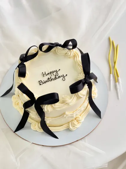 A vintage-style cake with a modern twist, featuring delicate piping and bold black ribbons. This design is a favorite for chic birthday celebrations.
