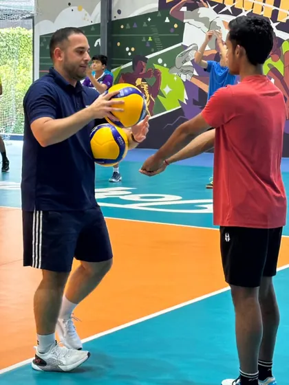 A coach provides hands-on instruction during a cross-training session with the Bengaluru Torpedoes volleyball team, focusing on skills that are transferable to badminton.