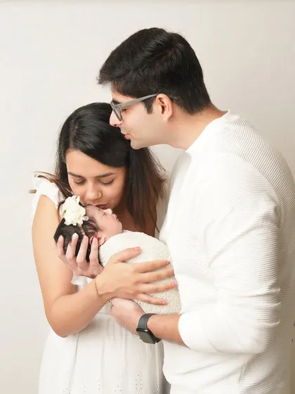A candid moment of love as parents kiss and hold their newborn baby. The all-white theme creates a bright, airy, and timeless family portrait.