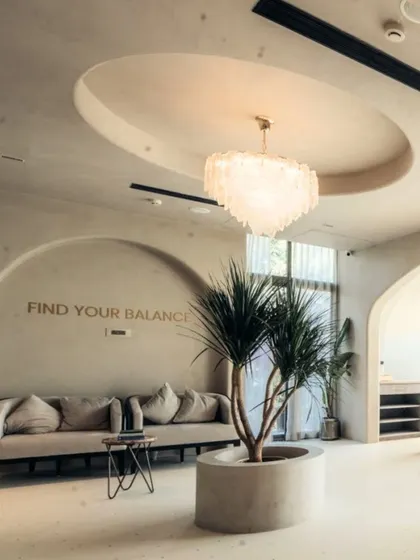 This lounge area in the studio is designed for quiet contemplation. The motto 'Find Your Balance' is subtly integrated into the wall, while the curved sofa, natural plant, and soft chandelier create a serene and welcoming corner.