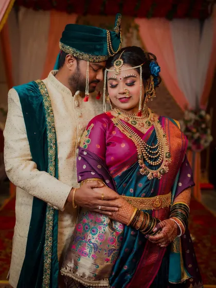 The rich colors of this couple's attire are stunning. The bride's deep purple and teal Paithani saree with traditional jewelry and the groom's elegant sherwani create a beautiful, classic Maharashtrian wedding portrait.