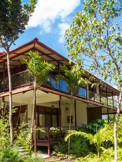 The stunning architecture of our Kabini resort, surrounded by palm trees and blue skies, promises a stay in sustainable elegance.